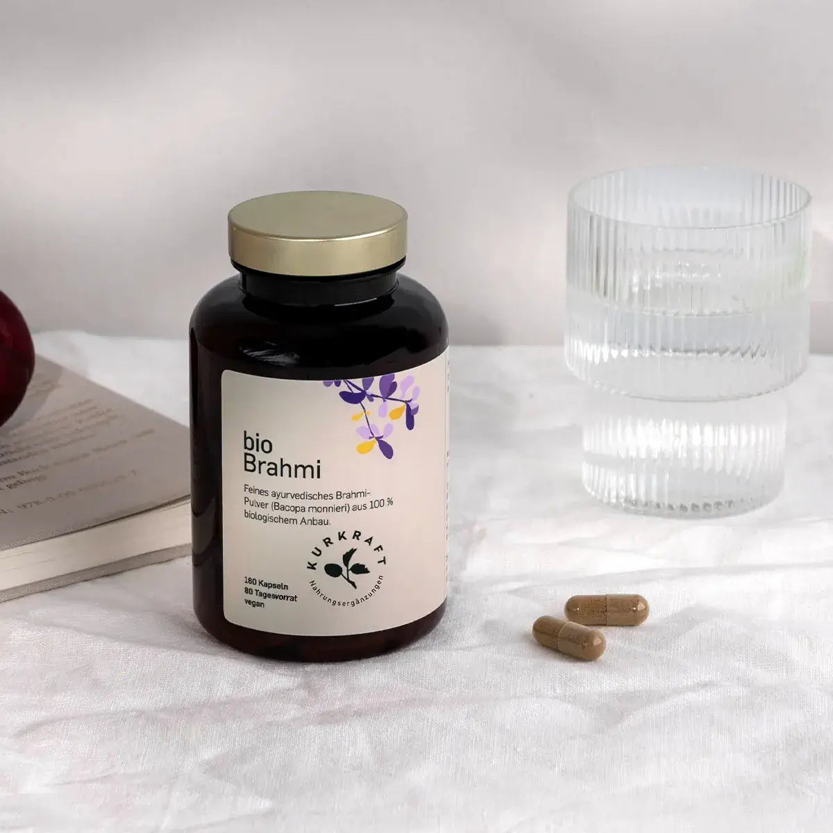 Zwei Bio Brahmi Kapseln neben einem Glas Wasser