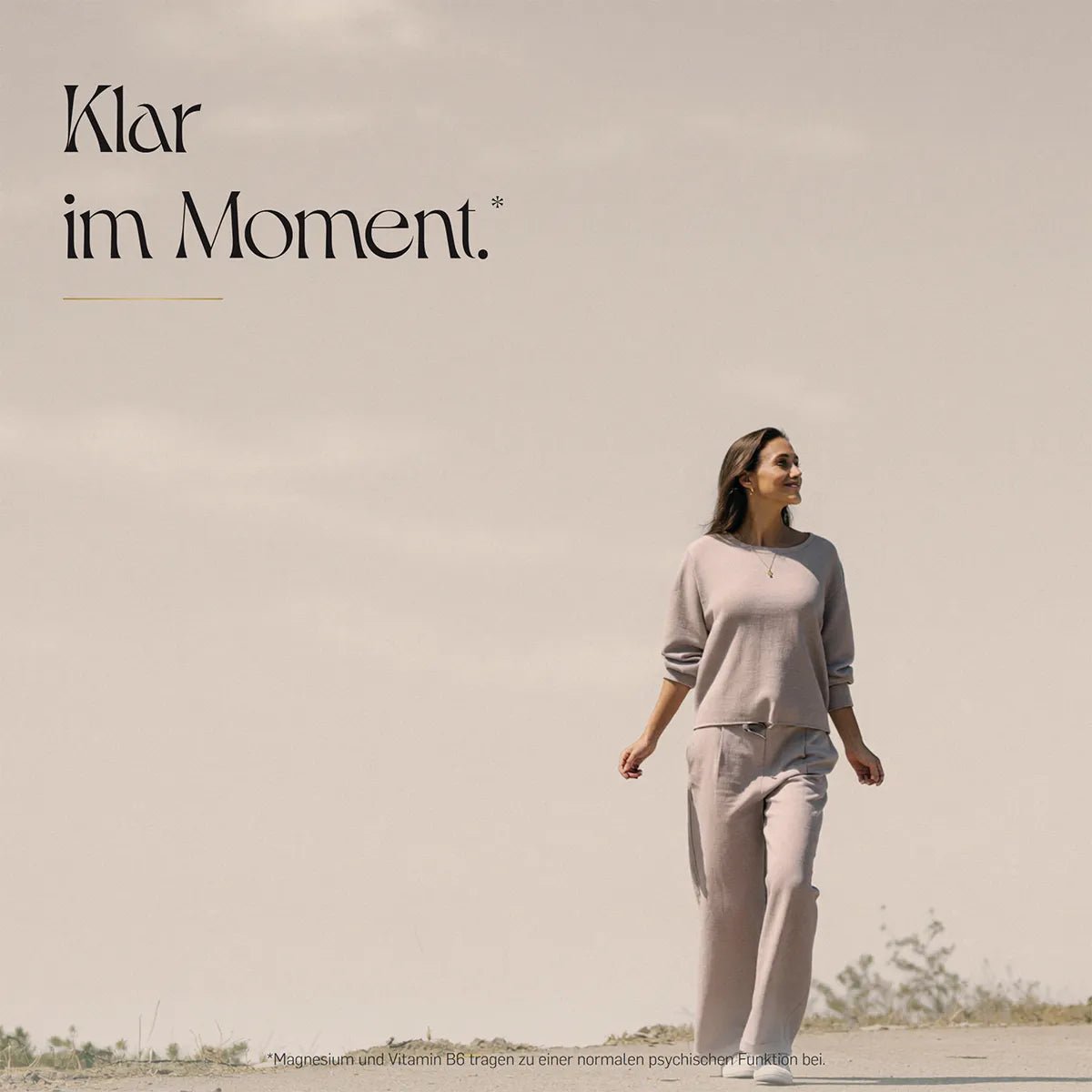 Klar im Moment – Frau in beigem Outfit geht entspannt durch eine helle Dünenlandschaft mit vereinzelten Gräsern unter weitem Himmel.