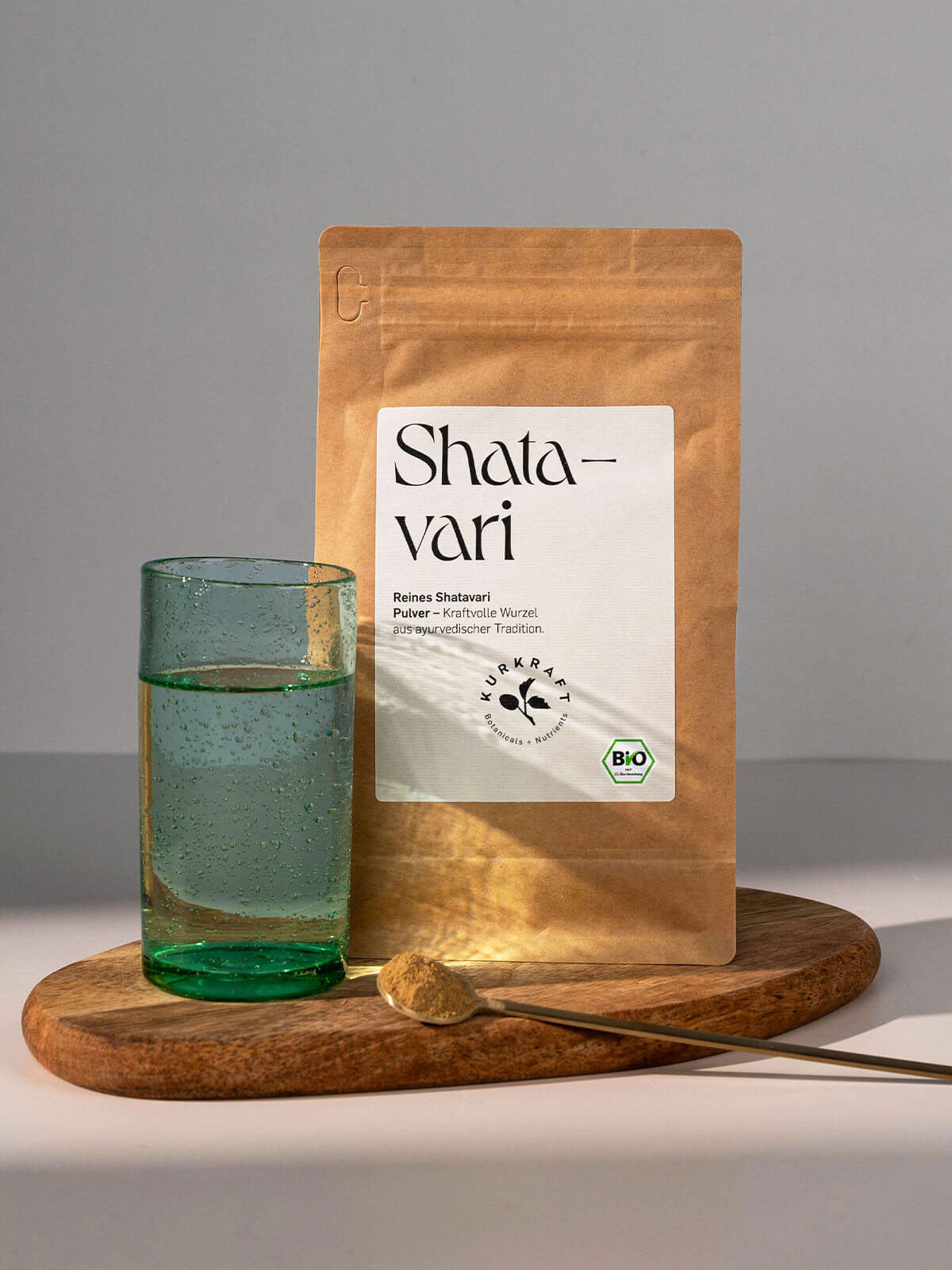 Shatavari Pulver im braunen Papierbeutel mit Glas Wasser und Löffel – ayurvedisches Naturprodukt für Balance und Wohlbefinden.