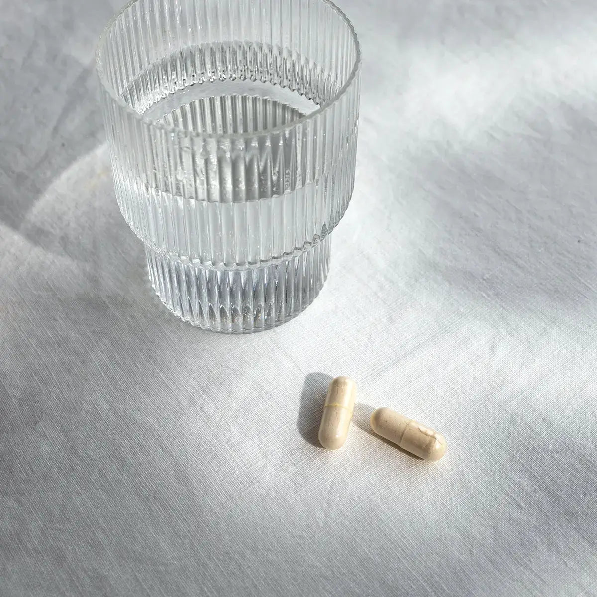 Zwei Wild-Yam-Kapseln neben einem Glas Wasser auf einem Tisch