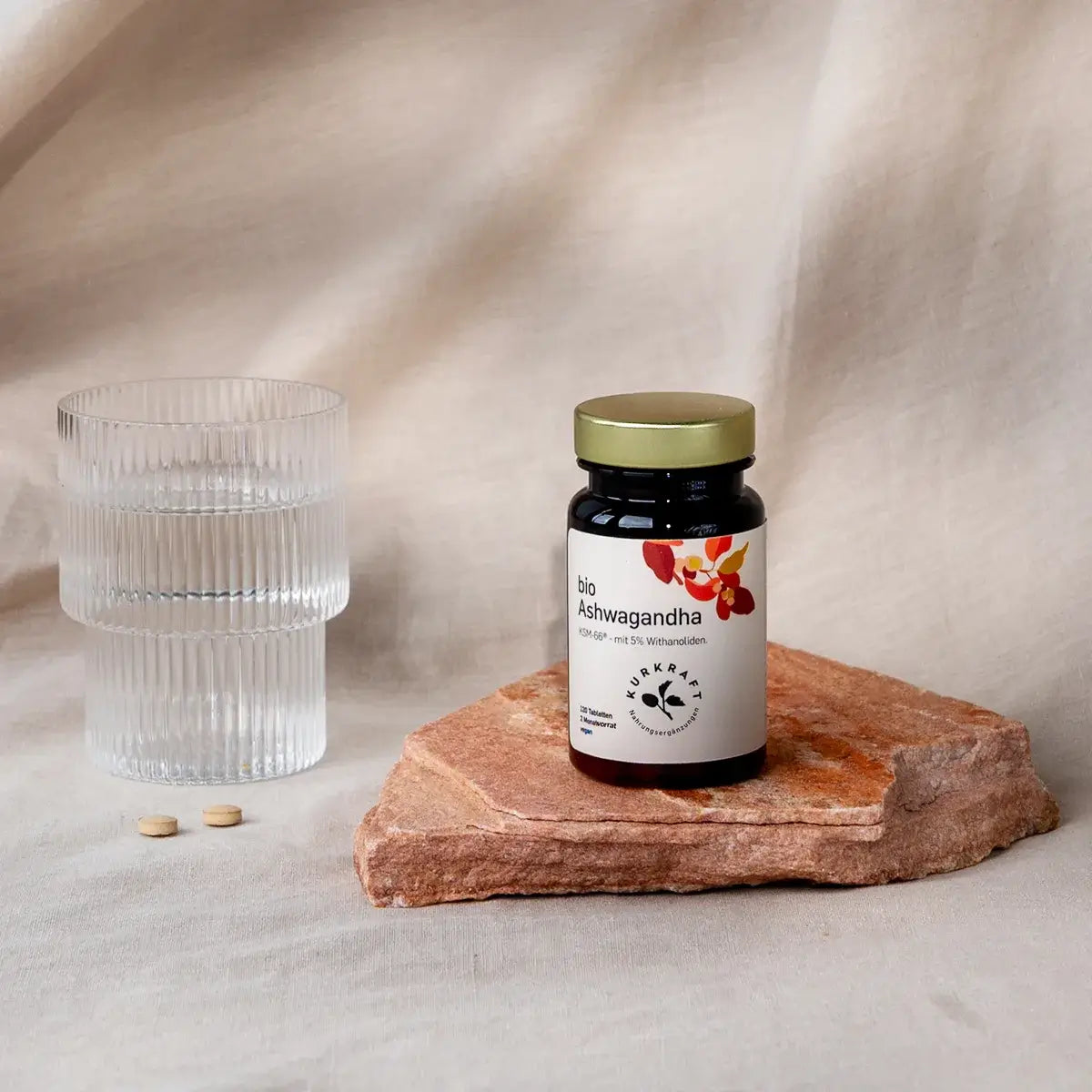 Zwei Bio Ashwagandha KSM-66 Tabletten neben einem Glas Wasser