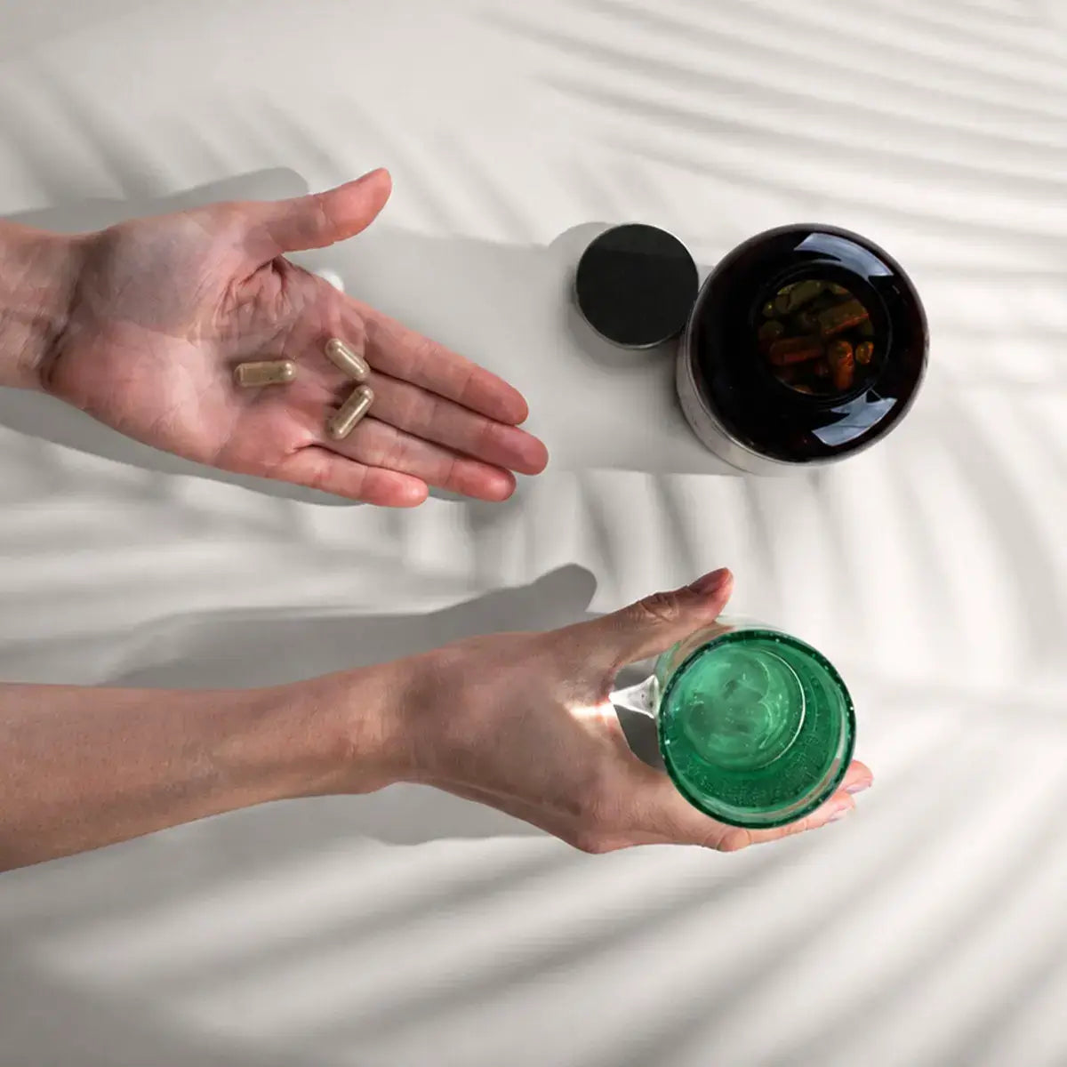 Bio Triphala Kapseln neben einem Glas Wasser auf hellem Untergrund
