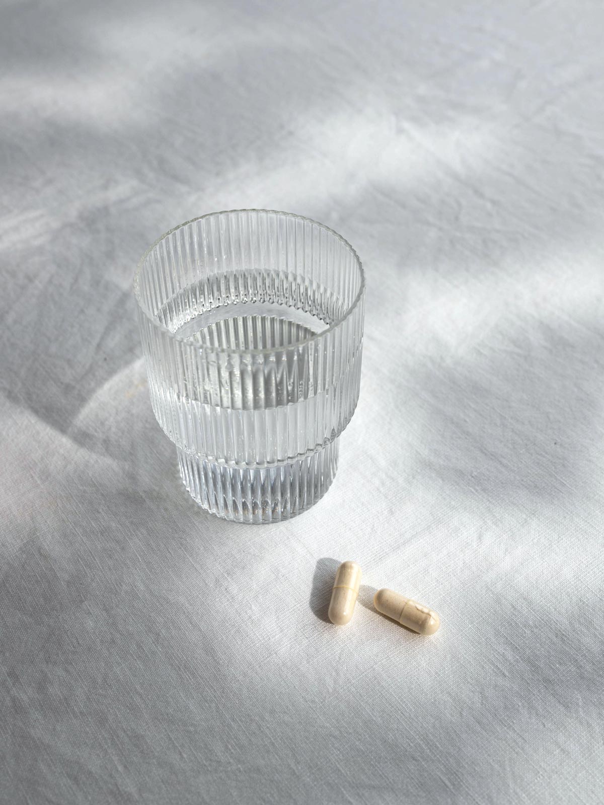 Zwei Kurkraft Triphala Kapseln mit Glas Wasser – ayurvedisches Ritual für tägliches Wohlbefinden.